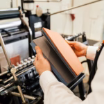 A person thumbs through a book recently printed by an offset printer, which is in the background of the image.