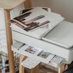 A cozy home office corner with a printer, coffee cup, and printed photos on a wooden table.