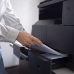 Woman loading paper into a large office laser printer.